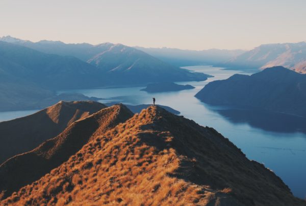 Photo of person standing on top of mountain peak looking over lake